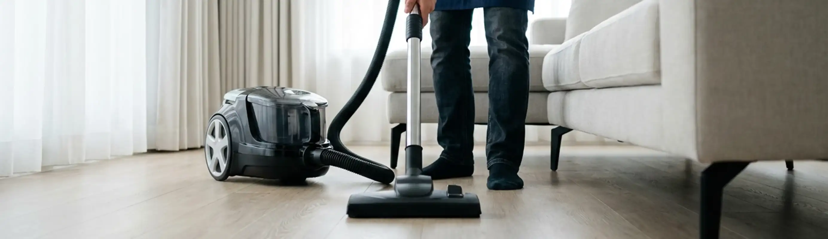 Professional house cleaner vacuuming a living room floor with a canister vacuum cleaner, Lakewood, CO.