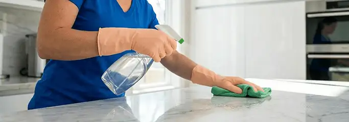 Maid service worker spraying and wiping a kitchen countertop with a microfiber cloth for sanitizing, Lakewood, CO.