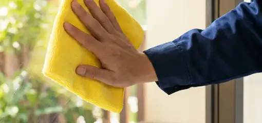 House cleaner wiping a glass window with a yellow microfiber cloth for streak-free cleaning, Lakewood, CO.